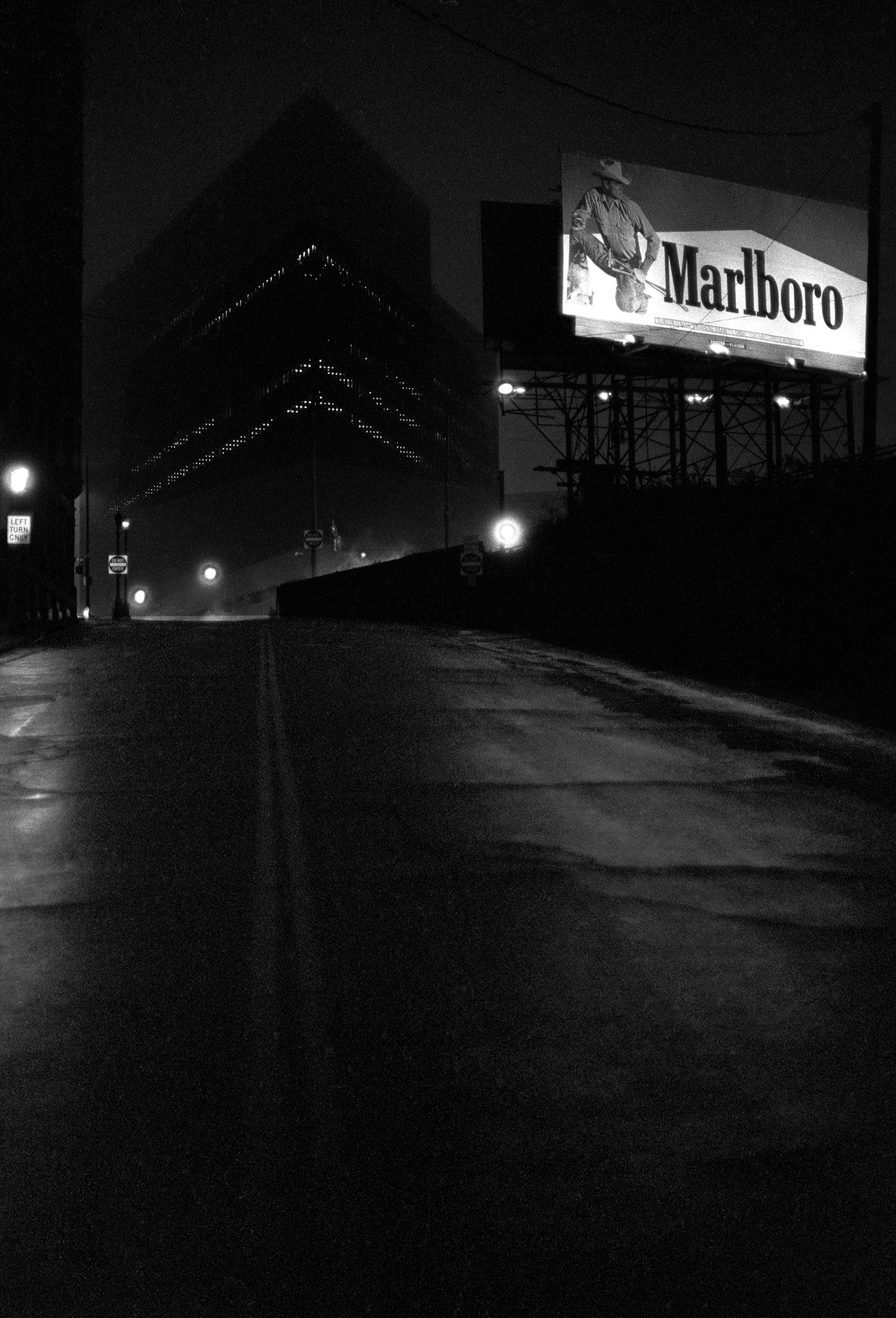 Black and white photograph of a Cleveland city street at night with a Marlboro advertisement in the background.