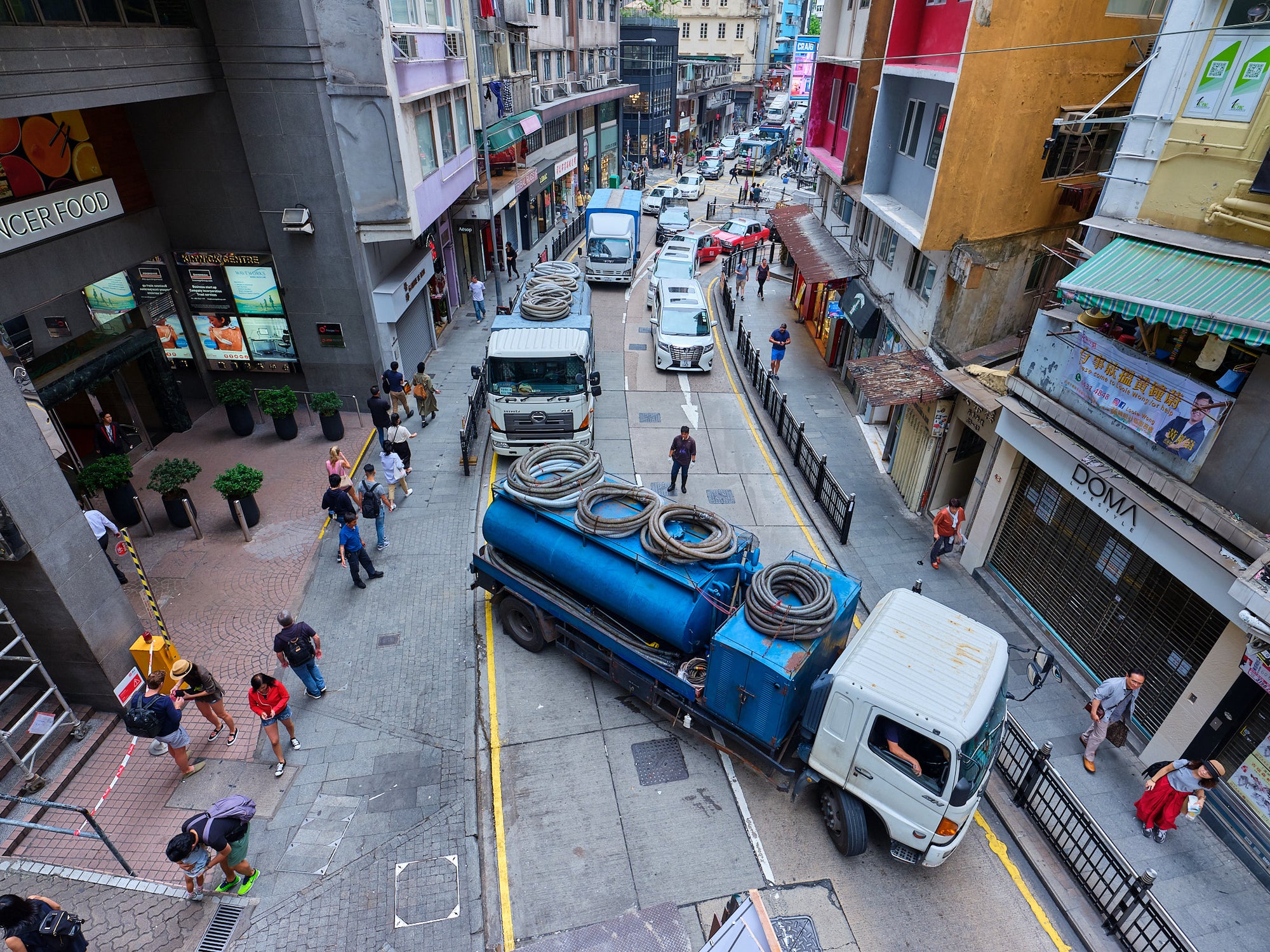 A blue truck is overturned on a busy Hong Kong street, with pedestrians and vehicles surrounding the scene.