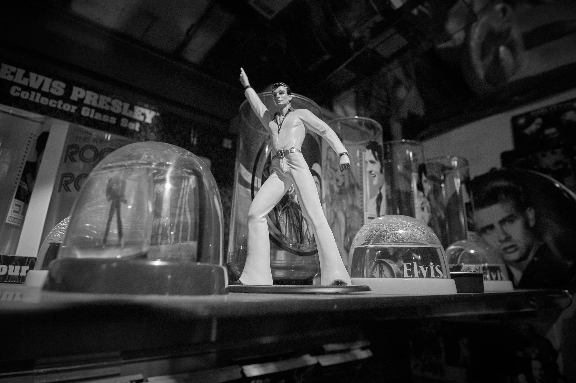 A figurine of Elvis Presley in a white suit pointing, displayed in front of a glass case with other collectibles.