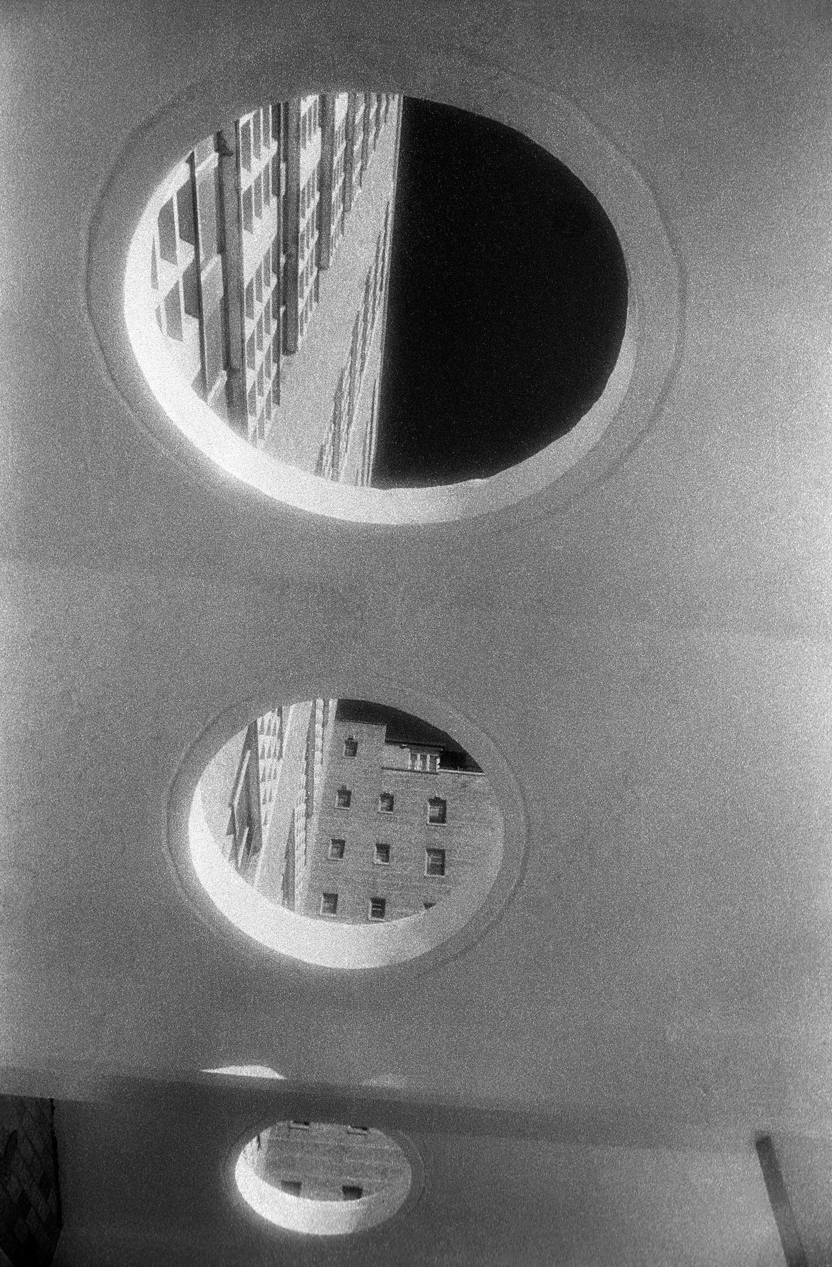 Three circular windows in a concrete wall with buildings.