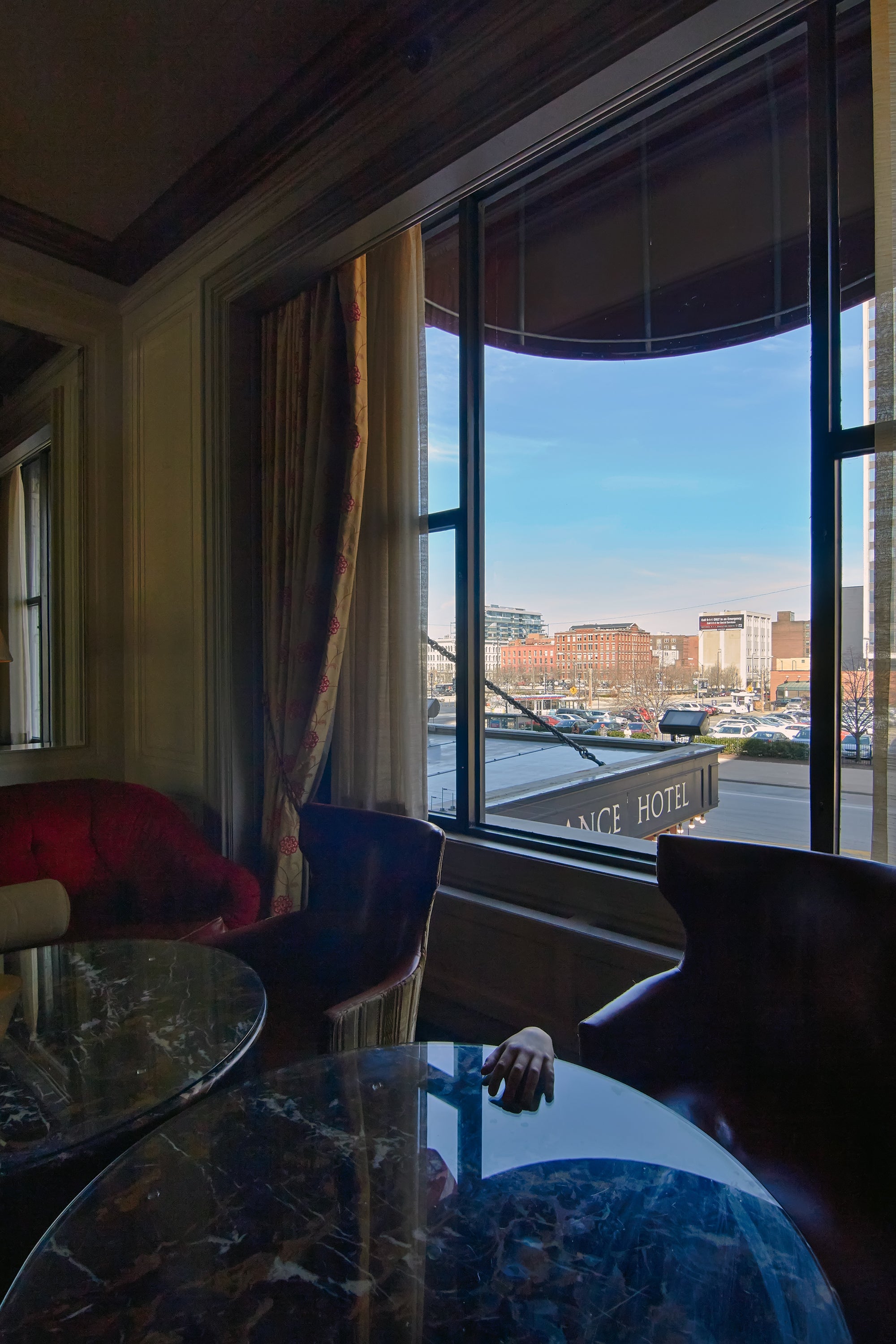Interior view of a room with a large window showcasing Cleveland cityscape, featuring a round table and chairs, curtains, and a view of buildings outside.