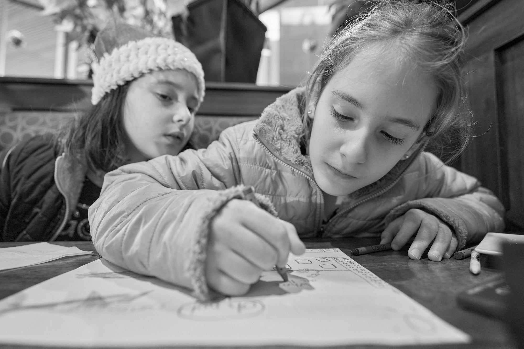 A black and white image of two children drawing at a table.