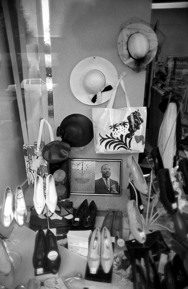 Storefront window featuring various shoes and hats and a clock with a picture of Dr Martin Luther King in Savannah GA in black and white.
