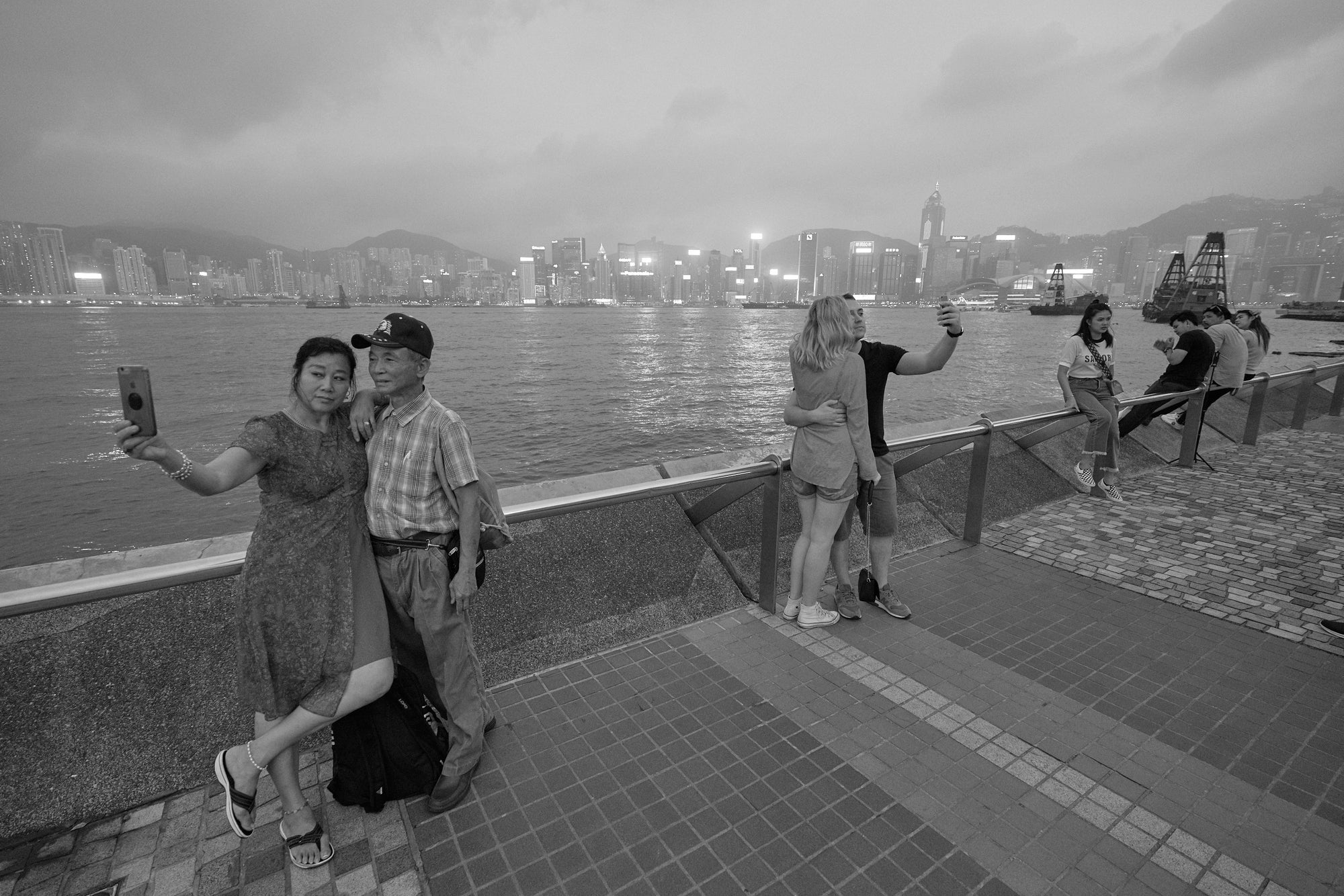 Black and white photograph of people taking selfies with Hong Kong's skyline in the background.