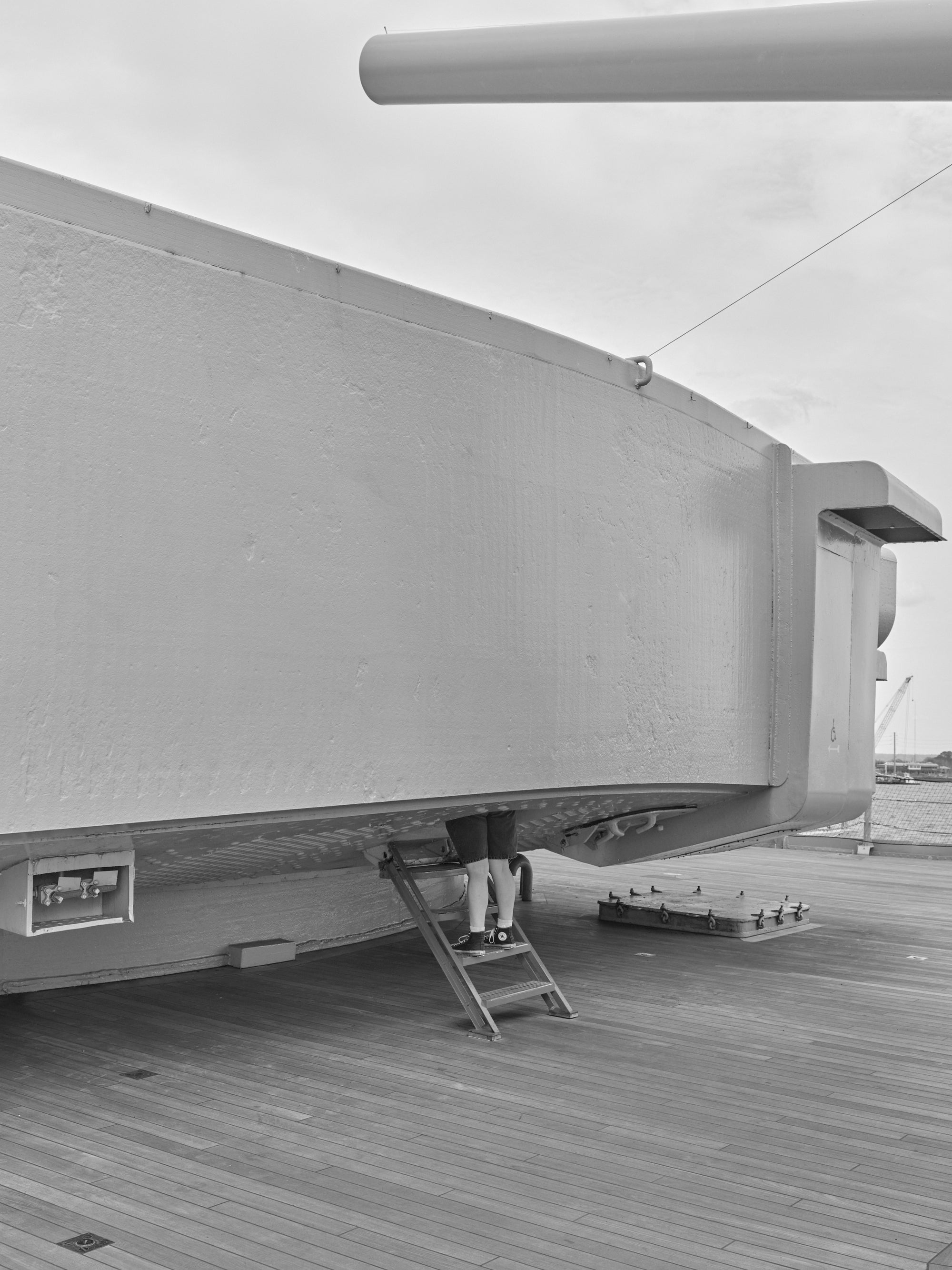 A black and white image showing the side of turret on the USS Alabama with a focus and two legs showing a visitor.