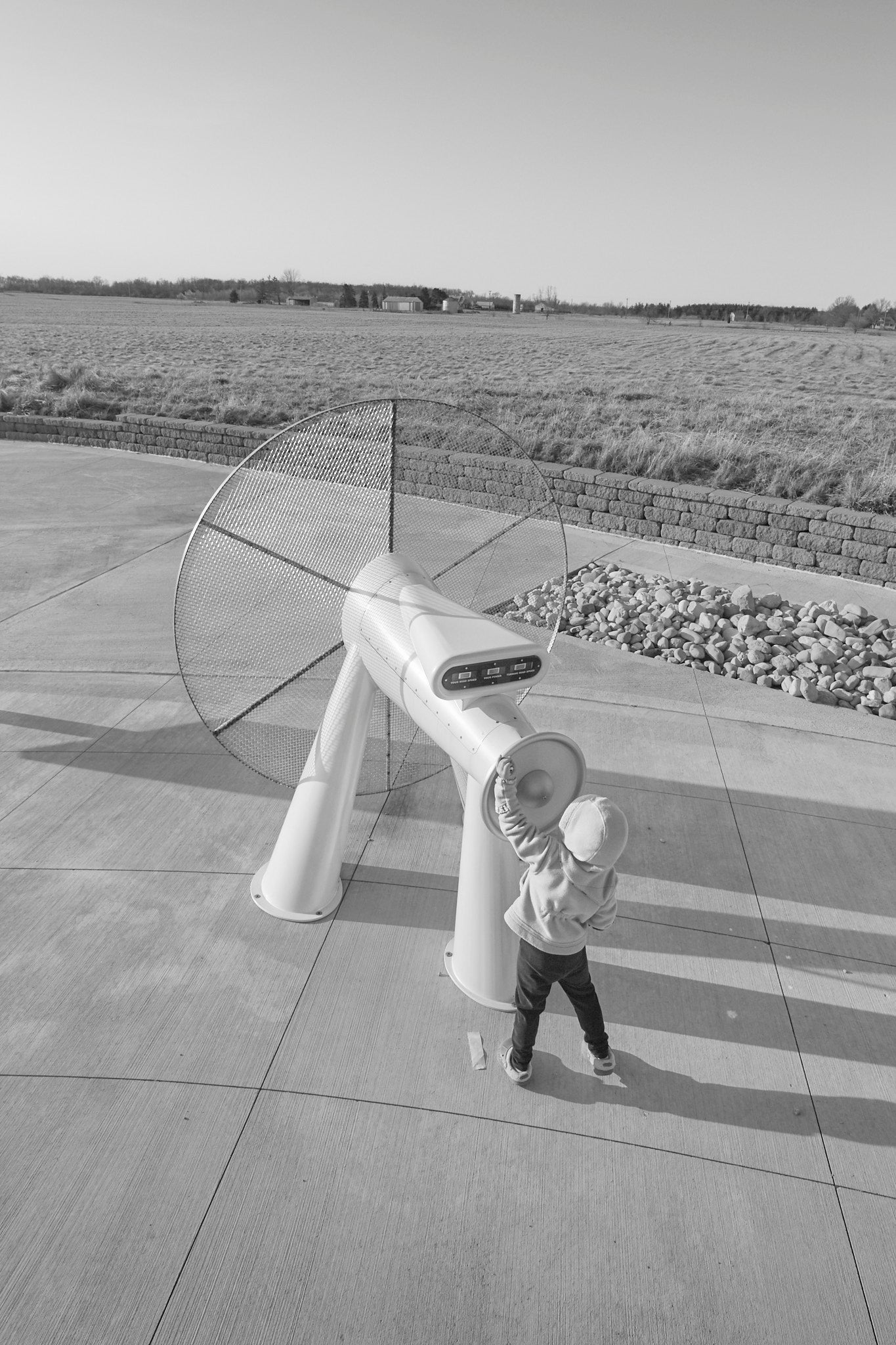 A large metal wind turbine sculpture positioned on a concrete floor with a small child standing next to it.