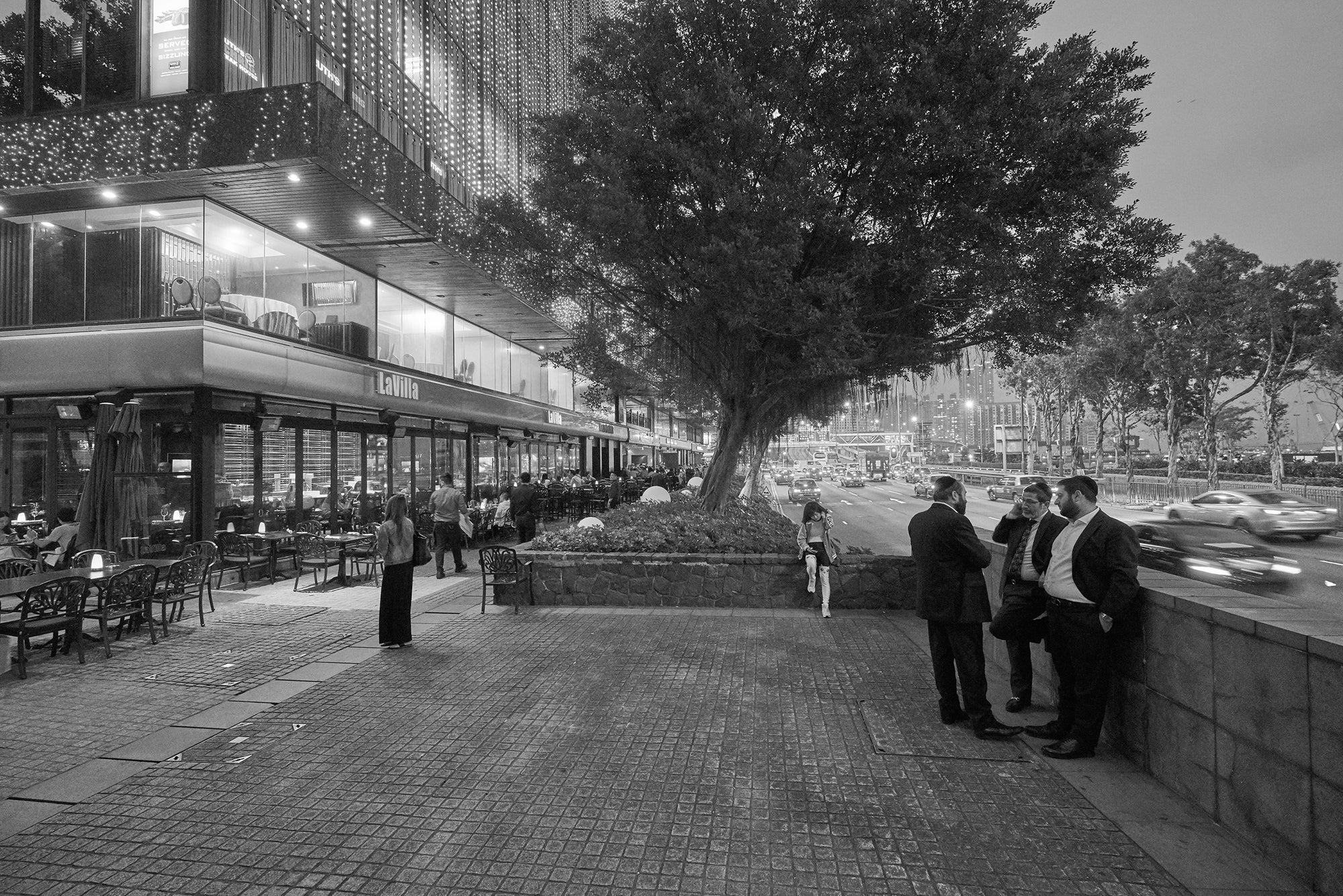 Black and white photograph of a street scene in Hong Kong featuring people and buildings.