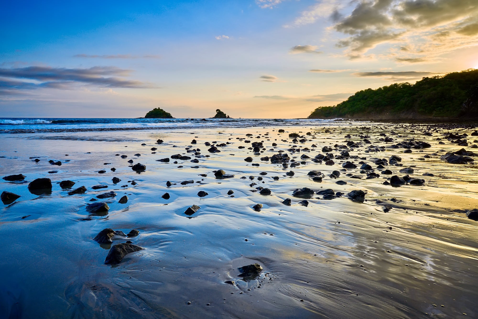 Sscattered rocks on Playa Danta Costa Rica beach at sunset with calm ocean at low angle.