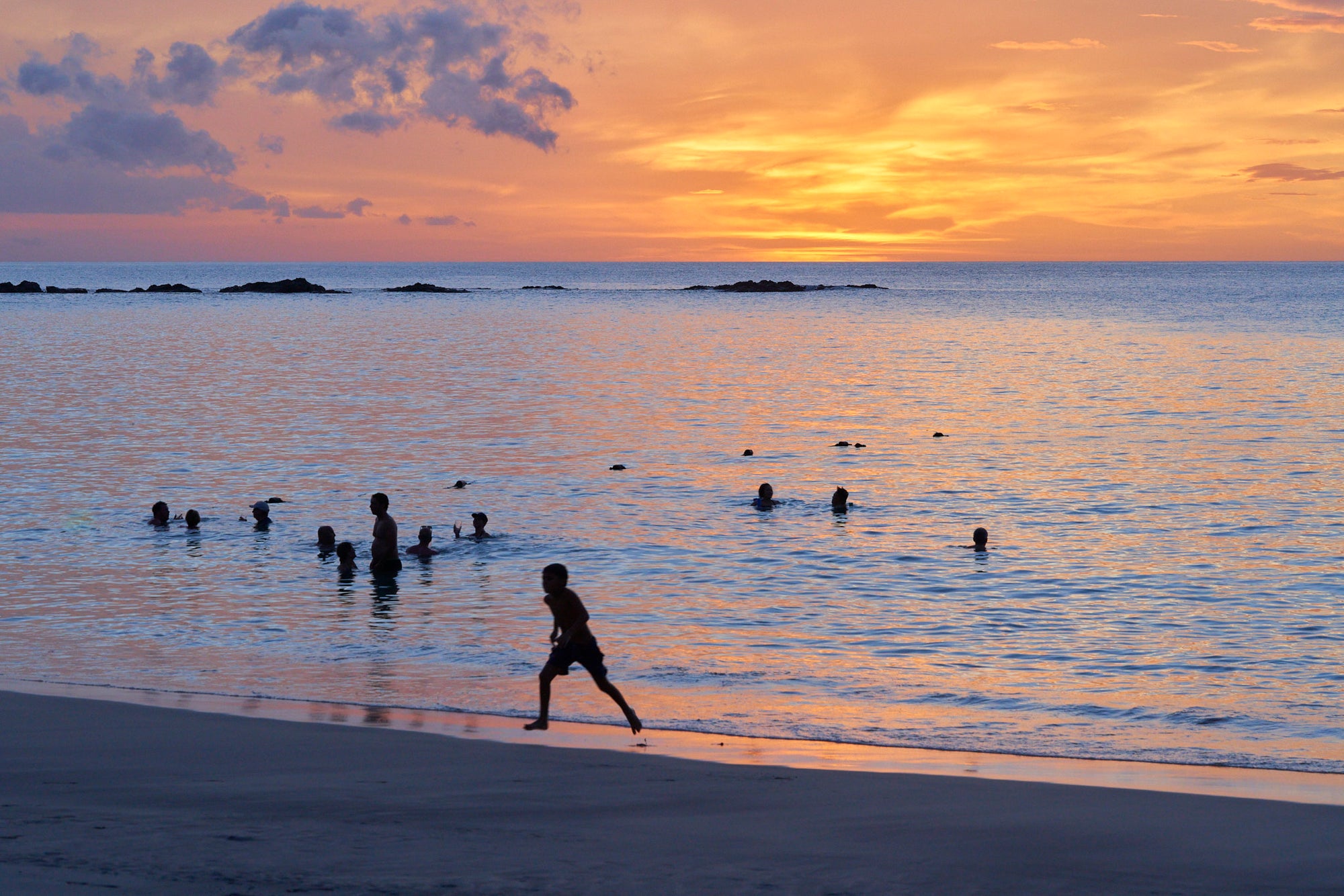 Tamarindo ocean sunset with silhouettes of people swimming against a vibrant sky.